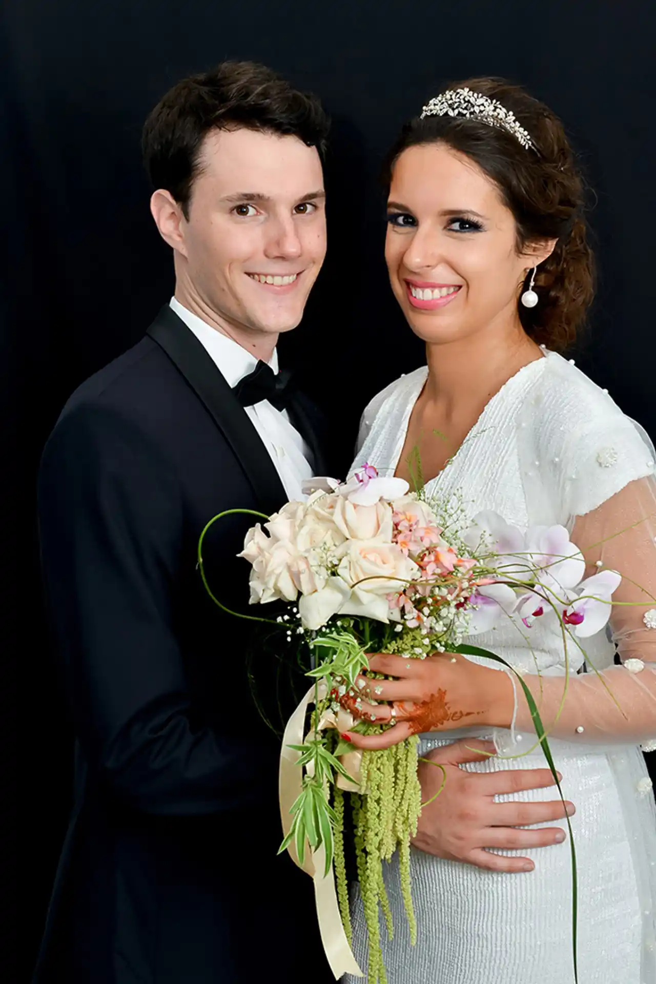 Jeune couple souriant en tenue de mariage, tenant un bouquet fleuri